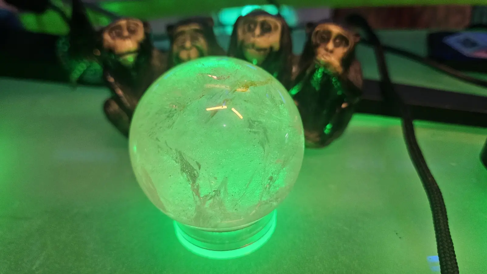 The crystal orb glowing green on a glass desk, with a row of carved monkey figures behind it.